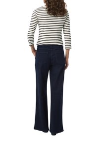 Dunkelblaue weit geschnittene Jeans mit einer glatten Denim-Oberfläche und zwei Gesäßtaschen. Kombiniert mit einem schwarz-weiß gestreiften Oberteil mit Dreiviertelärmeln.