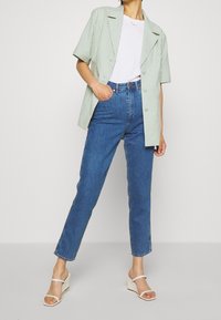 Zelená kostkovaná košile s krátkým rukávem, bílý tričko pod ní, modré džíny s vysokým pasem a bílé platformové sandály. Jednoduchý, čistý design.