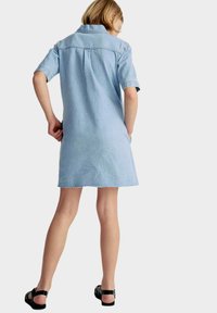 Hellblaues Denimkleid mit Kragen, kurzen Ärmeln und ausgefranstem Saum, kombiniert mit schwarzen Sandalen. Fokus auf lässigem, entspanntem Design.