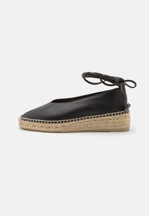 Musta nahkainen espadrille-tasapohjakengä, jossa on kudottu juuttipohja ja nilkan ympärille solmittava nauha, kuvattuna sivuprofiilista valkoisella taustalla.