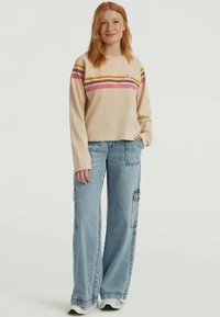 Beige sweater with multicolored horizontal stripes, paired with light blue wide-leg jeans featuring side pockets and a relaxed fit.
