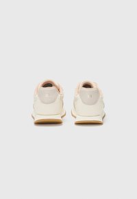 Hvite sneakers med rosa aksenter, glatt lærmateriale, rund form og strukturert gummisåle. Bakfra viser de minimal merkevare.