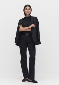 Svart skräddarsydd kavaj som hänger över axlarna, i kombination med en ribbad svart topp och svarta byxor. Slim-fit byxor, enkla svarta skor, minimala accessoarer.