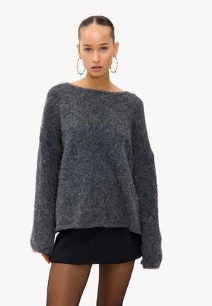 Pull en tricot gris et duveteux avec un large col bateau et des manches longues, associé à une mini-jupe noire. La texture semble douce et confortable.