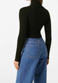 Black ribbed turtleneck with long sleeves, paired with high-waisted blue denim jeans featuring back pockets and a loose fit.