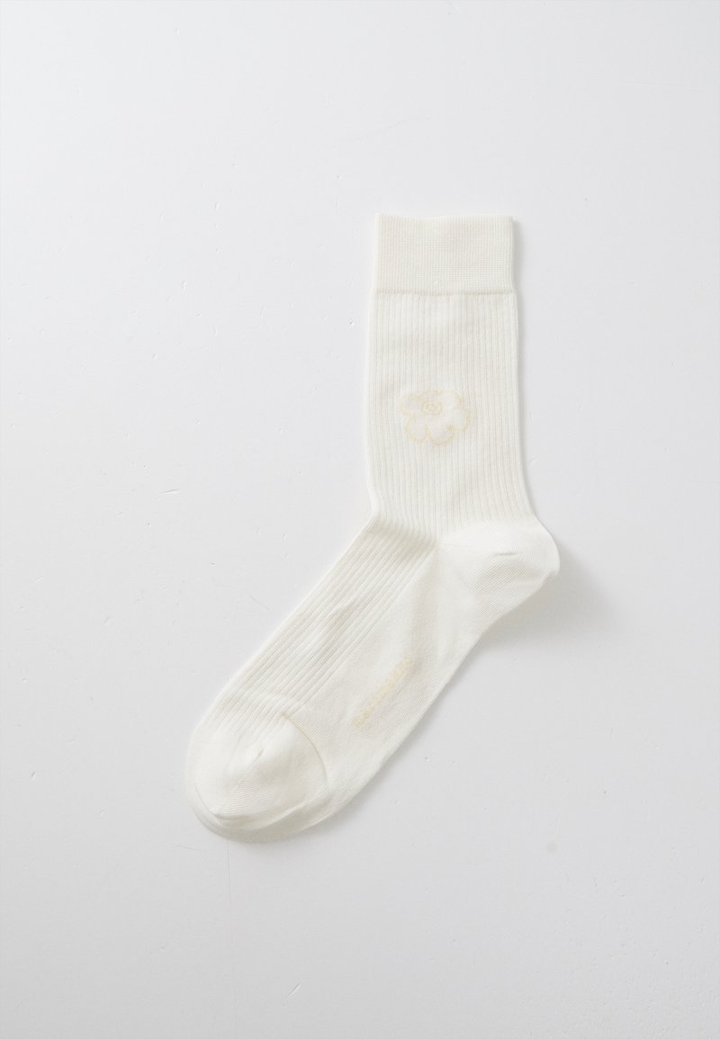 Calzino in cotone a coste color crema con un delicato motivo di fiori gialli sul lato. Il bordo è liscio, offrendo una vestibilità aderente nella parte superiore.