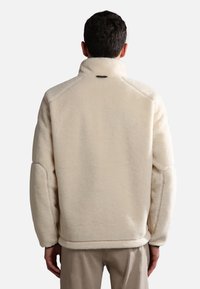 Cream-colored fleece jacket with a high collar, raglan sleeves, and smooth interior texture. Features a small logo near the collar.