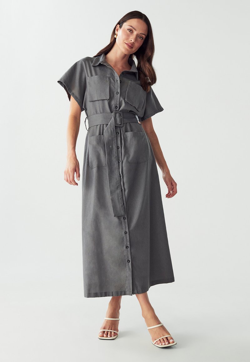 Robe chemise midi grise, à manches courtes, avec un devant à boutons, deux poches poitrine et une taille ceinturée. Tissu lisse avec une texture mate.