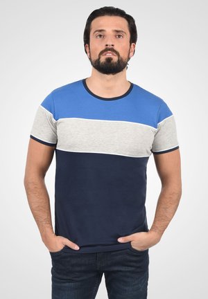 Majica kratkih rukava s horizontalnim prugama u plavoj, sivoj i tamnoplavoj boji s okruglim izrezom. Tkanina izgleda mekano; minimalistički dizajn.
