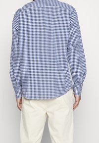 Blauw-wit geruite overhemd met lange mouwen, een gespreide kraag, knopenmanchetten en een gebogen zoom, gecombineerd met lichtbeige broeken.