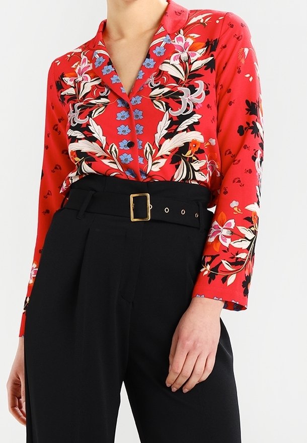 Red floral button-up blouse with long sleeves and a collar, featuring blue and white floral accents. Worn with high-waisted black trousers.