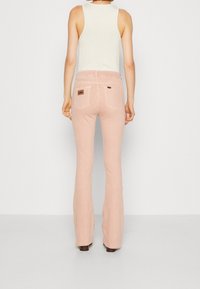 Vaaleanpunaiset, levenevät farkut, joissa on takalappu, kaksi taskua ja sileä pinta, yhdistettynä valkoiseen hihattomaan paitaan.