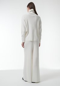 Witte, zachte gebreide outfit met een high-neck pullover en wijde broek, die een gladde textuur en een ontspannen pasvorm toont.