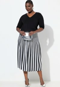 Zwarte v-hals trui gecombineerd met een knielange, geplooide zwart-wit gestreepte rok. Accessoires zijn een zilveren clutch en schoenen.