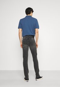 Camisa de polo navy, de manga corta, jeans grises, ajuste slim, dos bolsillos traseros con detalles de costura, combinada con zapatillas negras, vista desde la espalda.