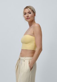 Yellow strapless top made of ribbed fabric, paired with cream striped high-waisted trousers. Side view highlights fit and design.