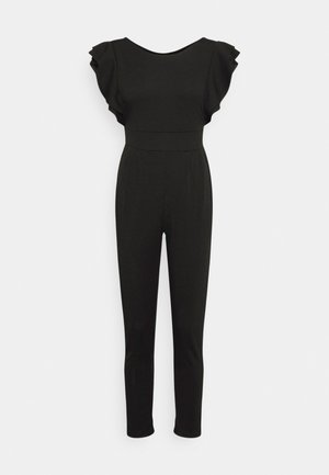 Zwarte aansluitende jumpsuit met vleermuismouwen, hoge taillenaad en taps toelopende broekspijpen tot op de enkel, tegen een effen witte achtergrond.