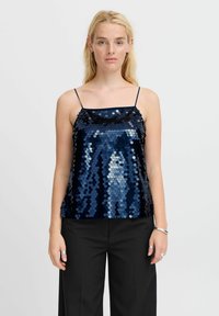 Camisole u tamnoplavim šljokicama s tankim naramenicama i lagano naboranim izrezom, uparen s crnim hlačama širokih nogavica. Glatka tekstura.