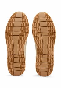 Suole di sneakers color beige chiaro con una superficie texture, caratterizzate da un motivo a scanalature ondulate e un marchio sul tallone.