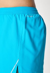 Turkise atletiske shorts med en tekstureret finish, der har en sidesplit og elastisk talje. Logoet er trykt nær taljen.