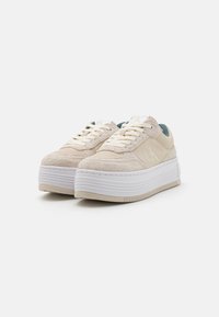 Sneakers platform beige con texture in suede, suola in gomma bianca, forma arrotondata e dettagli blu sul tallone, con design stringato e logo impresso.