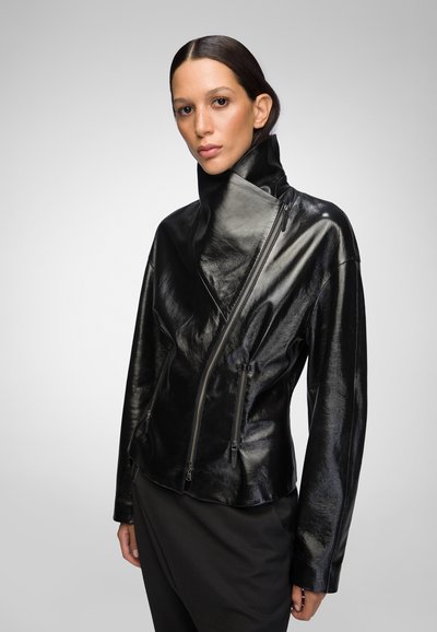 Black leather jacket with a high collar, asymmetrical zip closure, and a shiny finish. Long sleeves and fitted design with pockets.