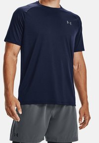 Laivastonsininen urheilupaita, valmistettu kosteutta siirtävästä kankaasta, pyöreällä kaula-aukkolla, lyhyillä hihoilla ja hillityllä logolla rinnassa.