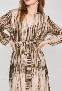 Abito lungo e fluido con un motivo beige chiaro e marrone scuro. Presenta una scollatura a V, maniche lunghe e una vita legata per una silhouette aderente.