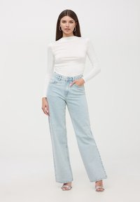 Maglietta bianca a maniche lunghe con colletto alto, abbinata a jeans a vita alta azzurri chiari a gamba larga con un delicato motivo a pois. Tacchi argento.