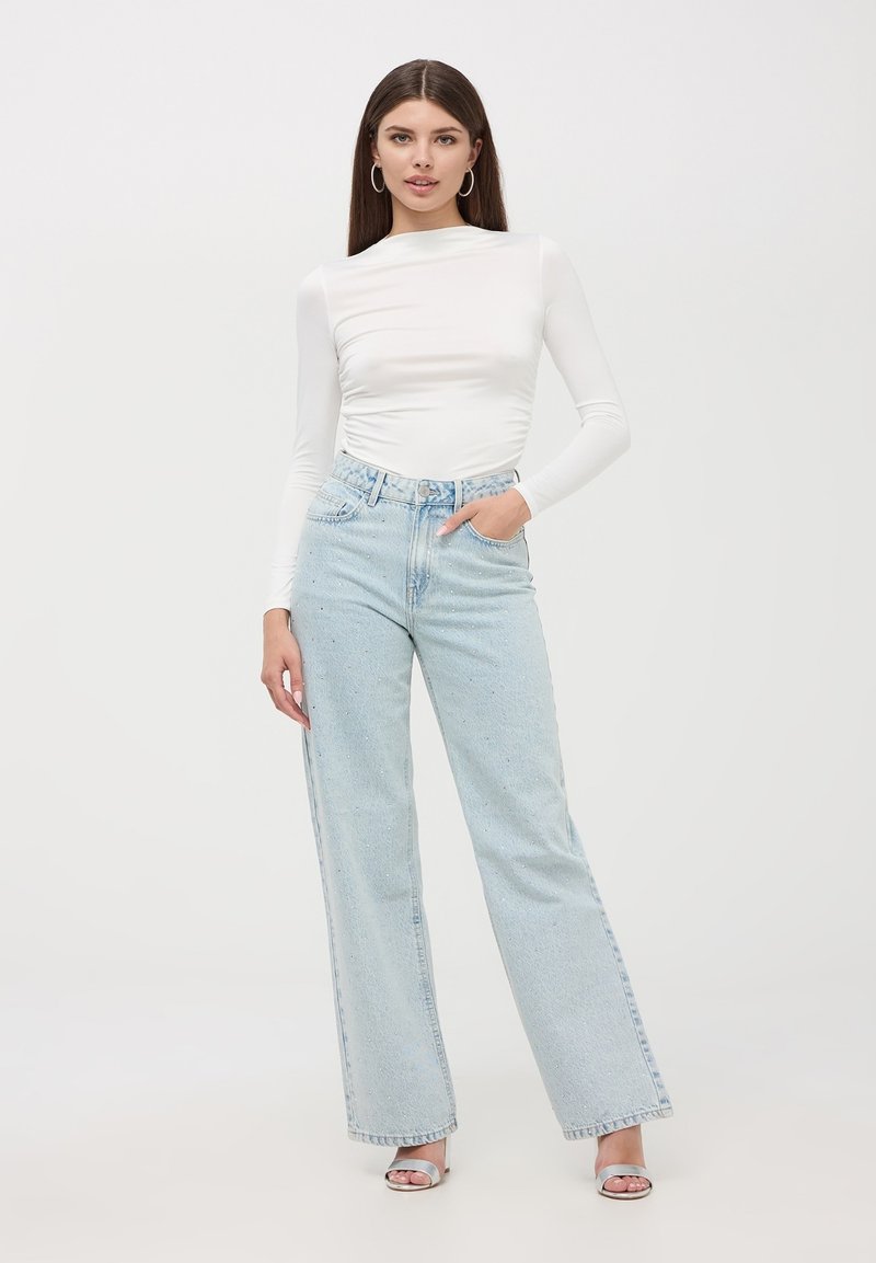 Maglietta bianca a maniche lunghe con colletto alto, abbinata a jeans a vita alta azzurri chiari a gamba larga con un delicato motivo a pois. Tacchi argento.