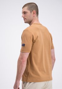 Majica s kratkimi rokavi in okroglim izrezom v bež bombažu, z modrim etiketom na levem rokavu in oranžnim poudarkom ob stranskem šivu.