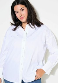 Camicia bianca con bottoni, realizzata in cotone e con un fit rilassato. Presenta decorazioni di paillettes sulle spalle e polsini classici.