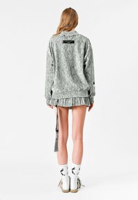 Sudadera gris de gran tamaño y textura con puños acanalados, combinada con una falda plisada. Complementada con calcetines blancos y zapatos con detalles verdes.