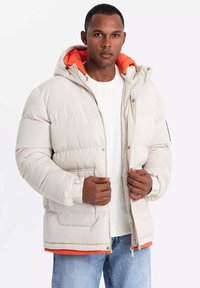 Vadderad jacka i ljusbeige med en orange insida, försedd med huva, dragkedjestängning och framfickor. Texturerad tyg med elastiska muddare.