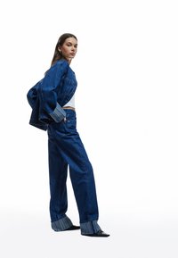 Chaqueta de denim con mangas anchas, combinada con jeans de pierna ancha de cintura alta, ambos en azul oscuro. El puño presenta un patrón de rayas en contraste.