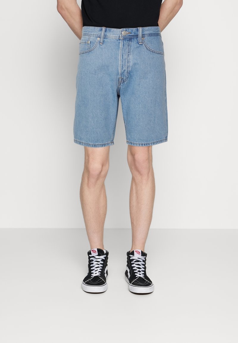 Ljusblå denimshorts med rak skärning, fem fickor och dragkedja, parat med svarta högstövlade sneakers.