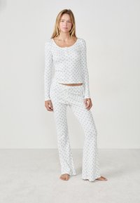 Witte lange mouwen top en flared broek set, met een blauw bloemmotief, zachte stof en een knoopsluiting bij de halslijn.