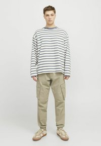 Gestreiftes Langarmshirt in Creme und Grau, kombiniert mit beigen Cargo-Hosen. Die Schuhe sind hellbraun mit einem dezenten Muster. Schlicht, lässige Passform.