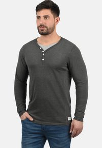 Mørkegrå langermet henley-skjorte med V-hals-design, som har tre hvite knapper på stigen og en grå indre krage.