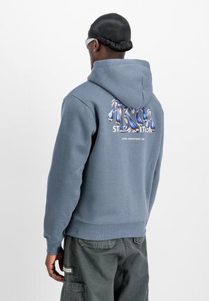 Grijze hoodie met een trekkoordcapuchon, voorzien van een meerkleurige graphic op de achterkant en geribde manchetten. Draagt over groene cargobroeken.