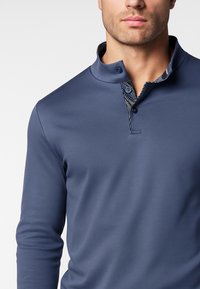 Polo a maniche lunghe color blu navy con una particolare patta a due bottoni e un colletto interno a contrasto con motivo decorato. Tessuto liscio e leggero.