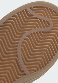 Semelle de chaussure marron avec motif cranté en zigzag texturé et incurvé pour adhérence et durabilité.