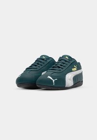 Roheline suede'i spordijalanõud valgete ja hallide aktsentidega, millel on paeltega disain ja tekstureeritud tallad. Vasakul jalal on kollane Puma logo.