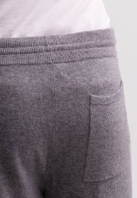 Graue Lounge-Hose aus einem weichen, strukturierten Stoff, mit einem gerippten Bund und einer kleinen Tasche auf der Rückseite.