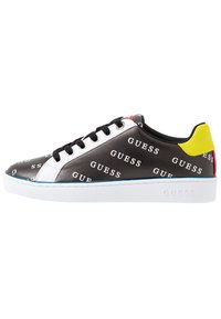 Baskets noires avec des accents blancs et un motif de logo "GUESS", dotées de lacets noirs, d'une surface texturée, d'une semelle blanche et d'un détail de talon jaune.