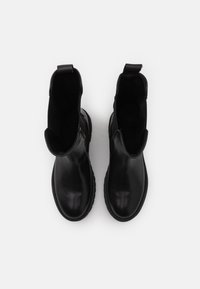 Botas de cuero negras hasta el tobillo con paneles elásticos en los laterales, puntera redondeada y suela texturizada. Sin marcas ni detalles de hardware visibles.