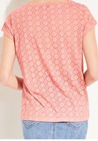 Lyserød mønstret top med et geometrisk design, korte ærmer og en afslappet pasform, parret med blå denim jeans.