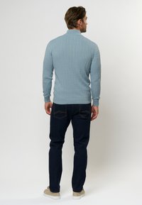 Šviesiai mėlynas megztinis su tekstūrinėmis vertikaliomis juostelėmis, su banguotu apykakle ir rankogaliais, derinamas su tamsiomis džinsomis ir šviesiais kasdieniškais batais.