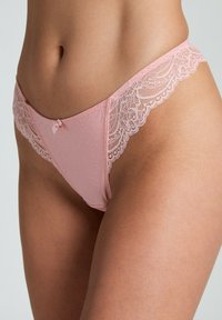 String rose clair avec des délicates bordures en dentelle et un petit nœud en accent. Tissu doux arborant des motifs en points texturés.
