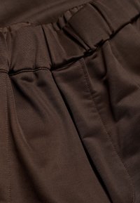 Gros plan sur un tissu brun foncé avec une ceinture élastique froncée et des plis cousus sur un pantalon ou une jupe.